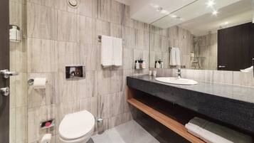 A modern bathroom with a marble wall, a black countertop sink, a white toilet, and a large mirror.