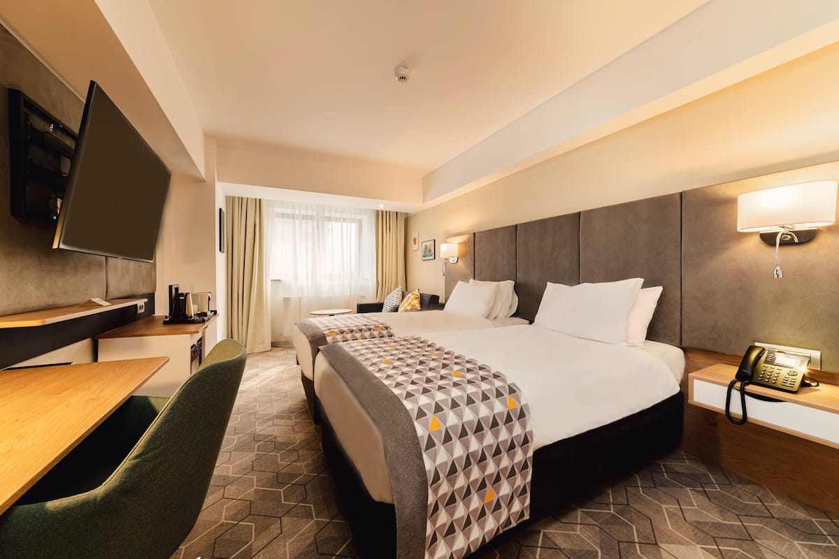 A hotel room with a large bed, a desk, a chair, a TV, and a phone on the bedside table.