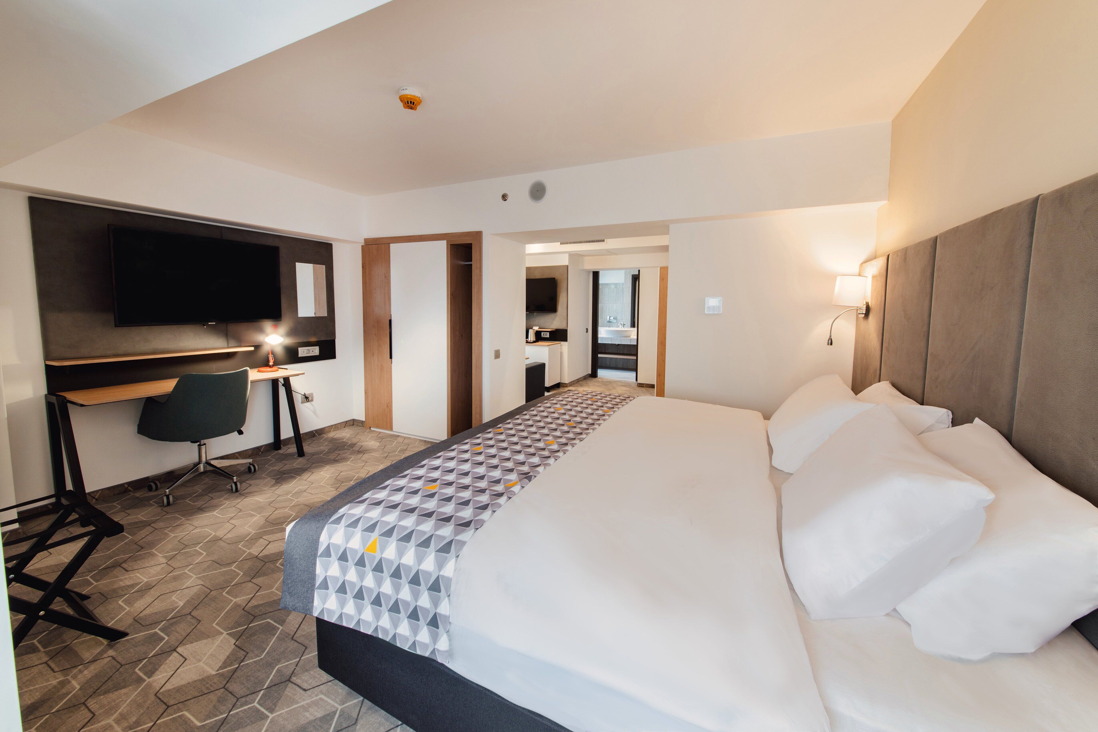 Een hotelkamer met een groot bed, een bureau met een stoel, een flatscreen televisie en een badkamer zichtbaar door een geopende deur.