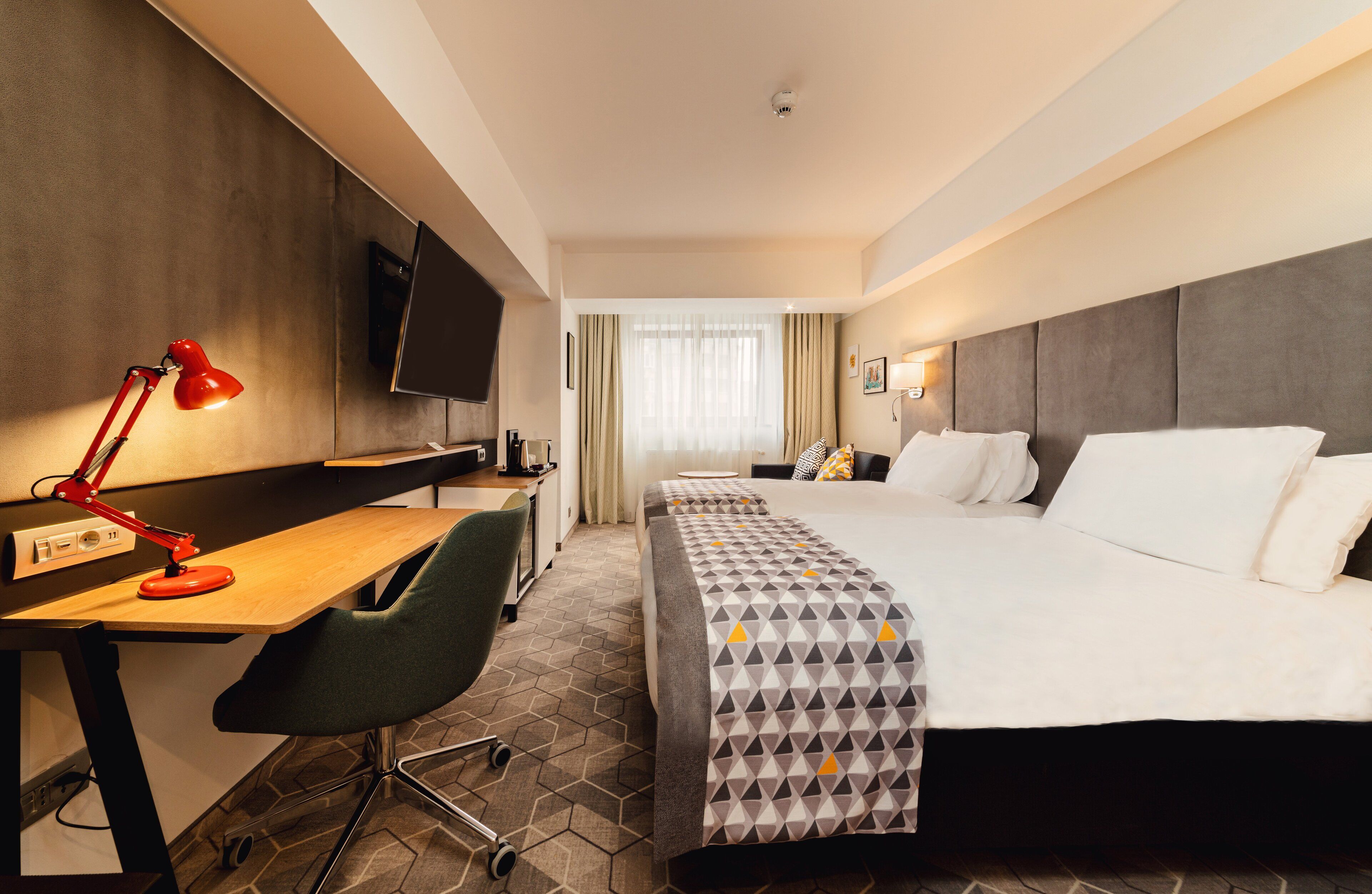 A hotel room with a bed, desk, chair, TV, and a window with curtains.