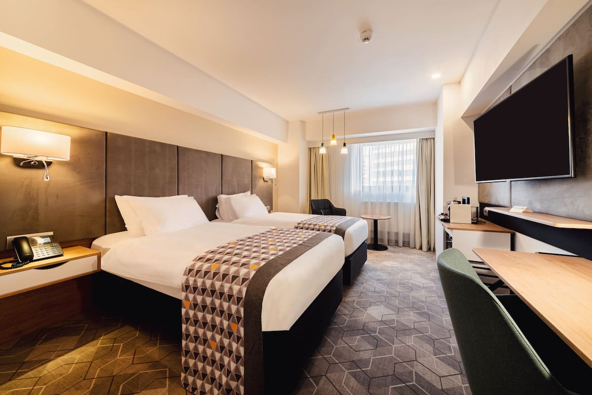 A hotel room with two beds, a desk, a chair, a TV, and a phone on the nightstand.