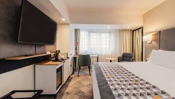 Une chambre d’hôtel avec un lit, un bureau, une chaise, une télévision et une fenêtre avec des rideaux.