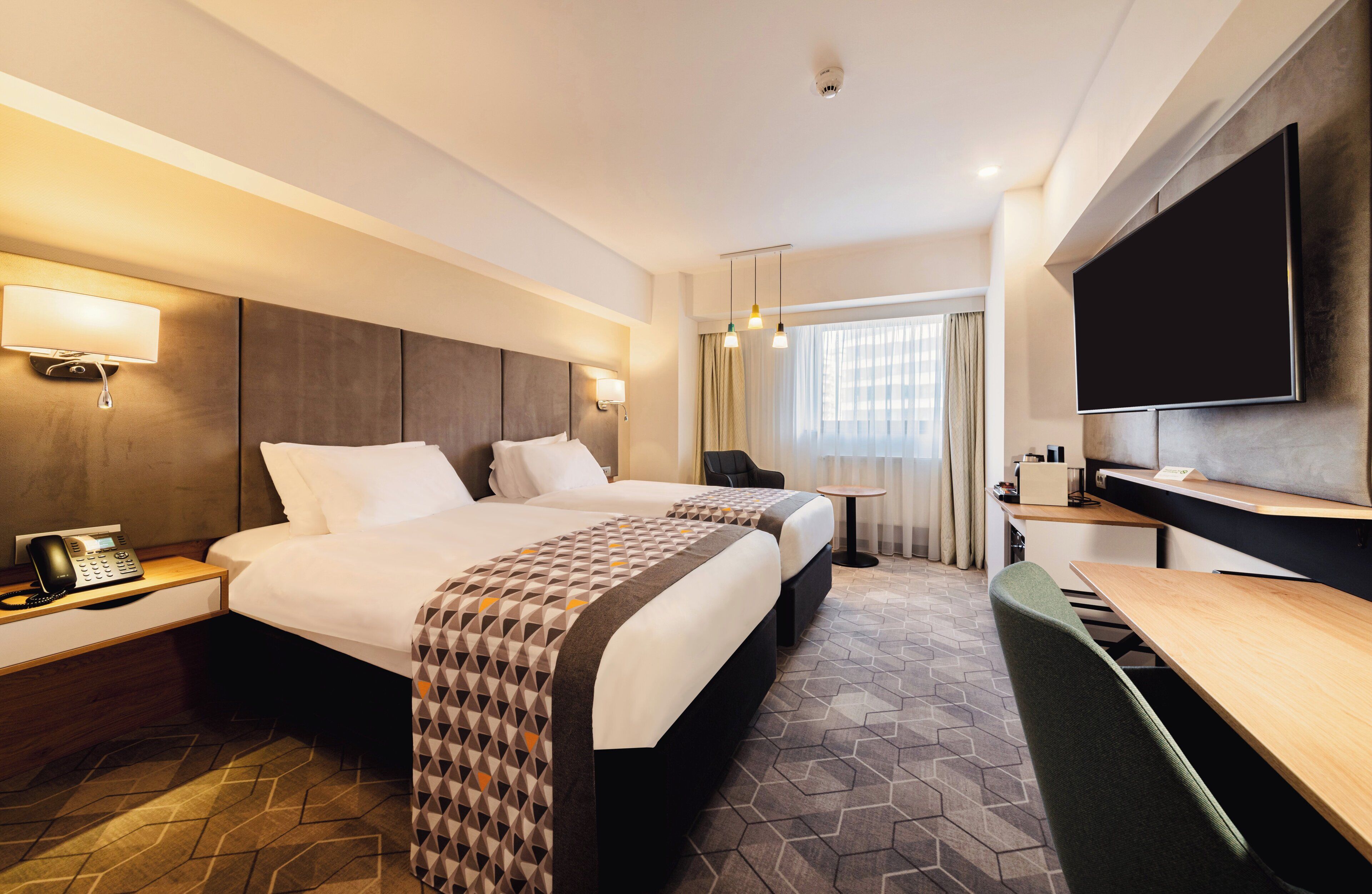 A hotel room with two beds, a desk, a chair, a flat-screen TV, and a telephone on the nightstand.