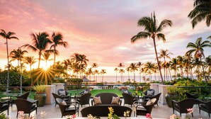 A rooftop lounge with outdoor seating, surrounded by palm trees and a view of the ocean at sunset. - Fairmont Orchid Gold Experience (Kamuela)