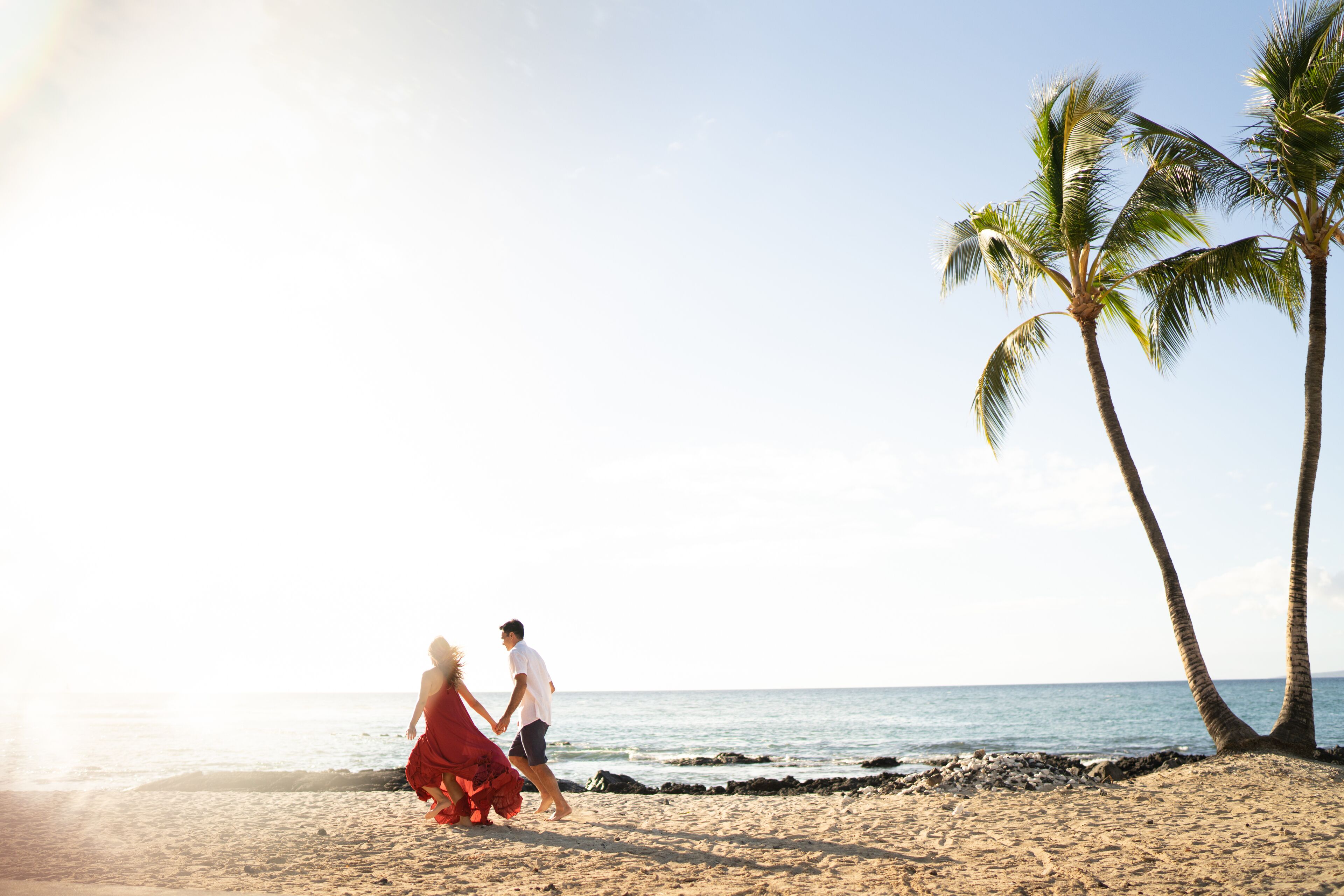 Escena de playa con una pareja caminando de la mano, palmeras y el océano.
