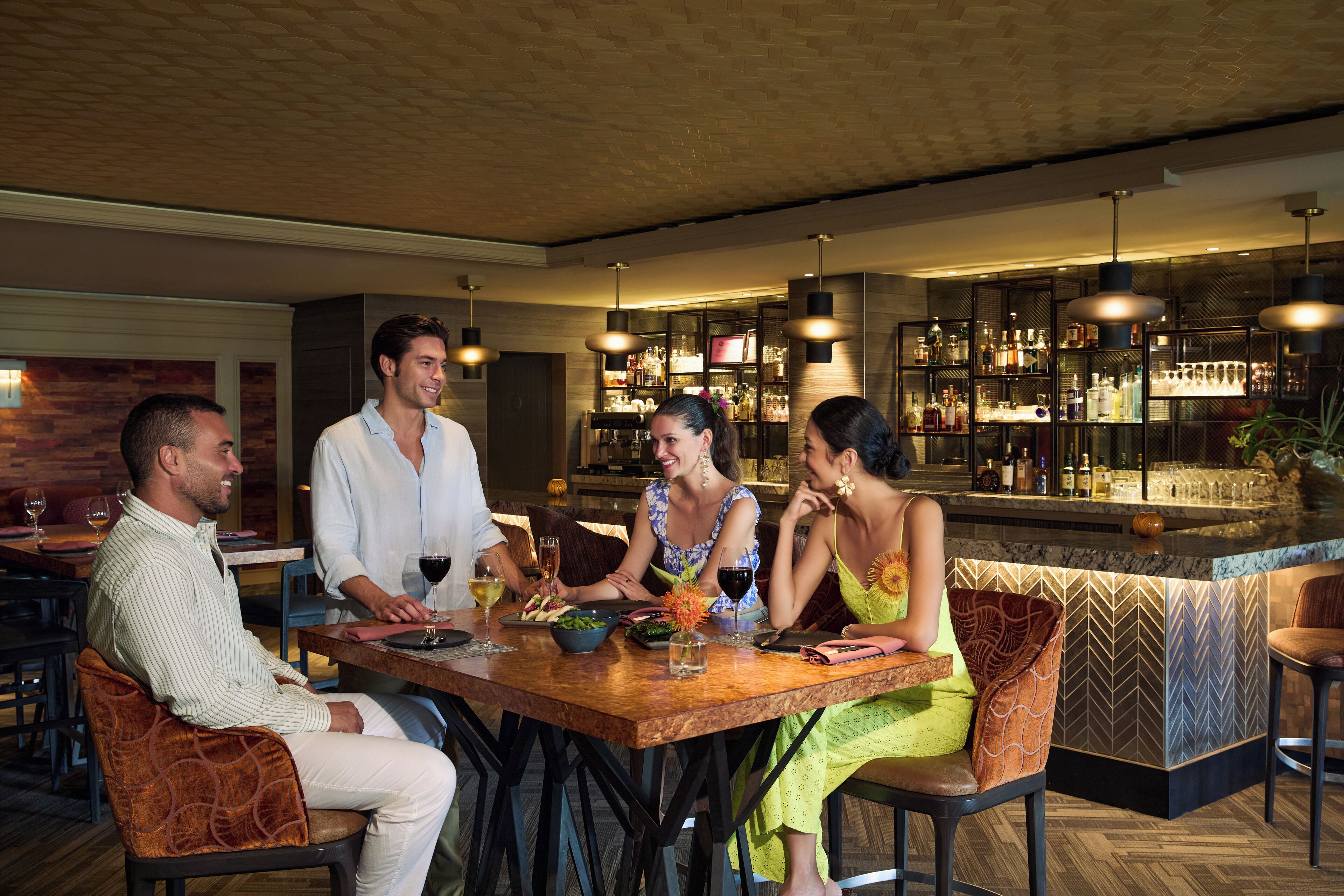 Un gruppo di persone sedute a un tavolo di legno in un ristorante, con un bar sullo sfondo.