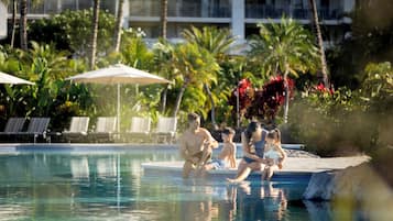 A swimming pool with lounge chairs and umbrellas, surrounded by palm trees and a hotel building.