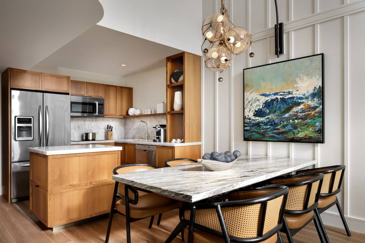 A modern kitchen with wooden cabinets, stainless steel appliances, a marble island, and a dining area with wicker chairs.