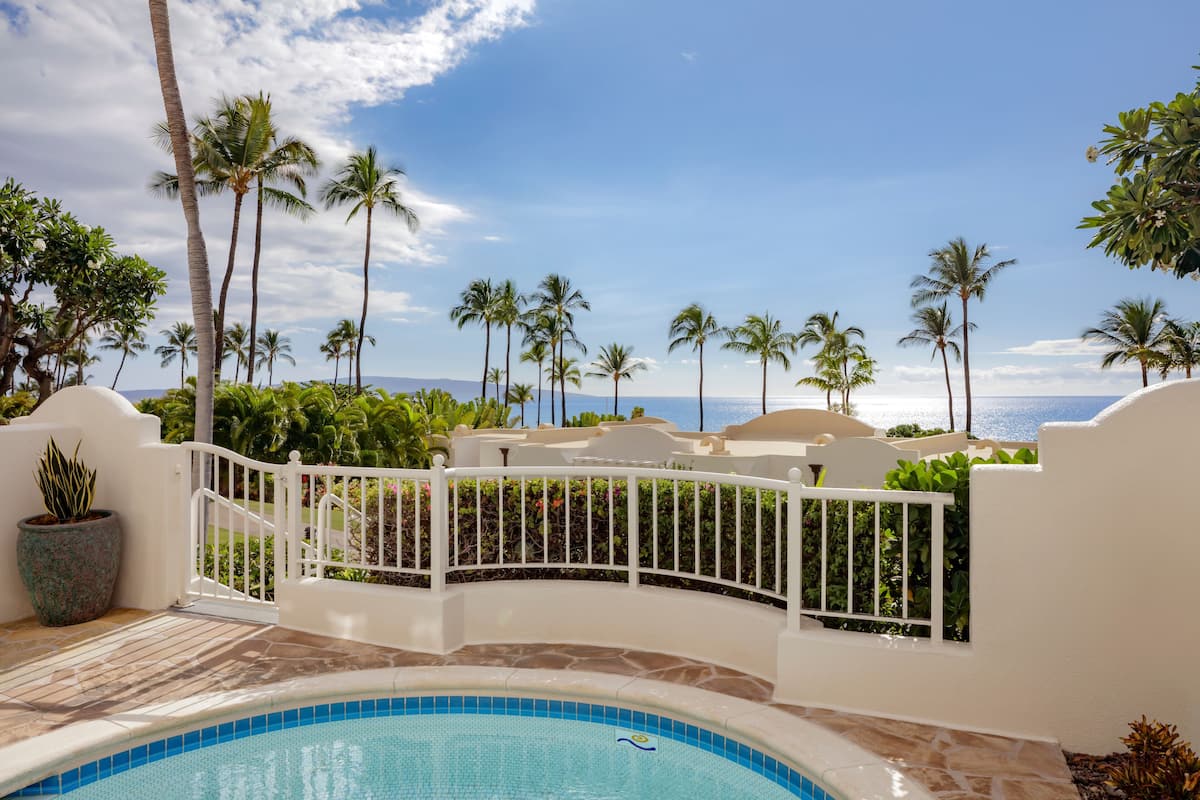A pool area with a view of the ocean and palm trees.