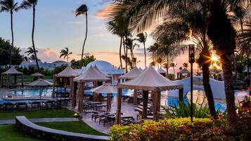 A resort pool area with lounge chairs, umbrellas, and palm trees.