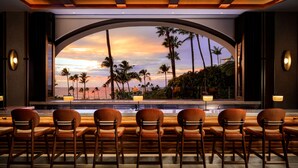 A hotel lobby with a large arched window overlooking a beach, several wooden chairs, and ambient lighting. - Fairmont Kea Lani Maui Villa Experience (Kihei)