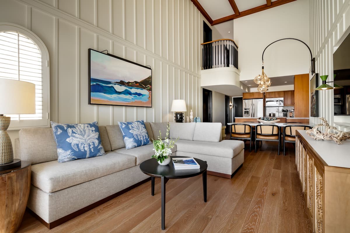 A modern living room with a sofa, coffee table, and artwork. A kitchen is visible in the background.