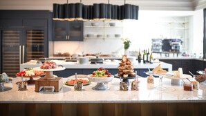 Una cocina moderna con encimera de mármol que exhibe una variedad de alimentos, entre ellos quesos, frutas y pan.