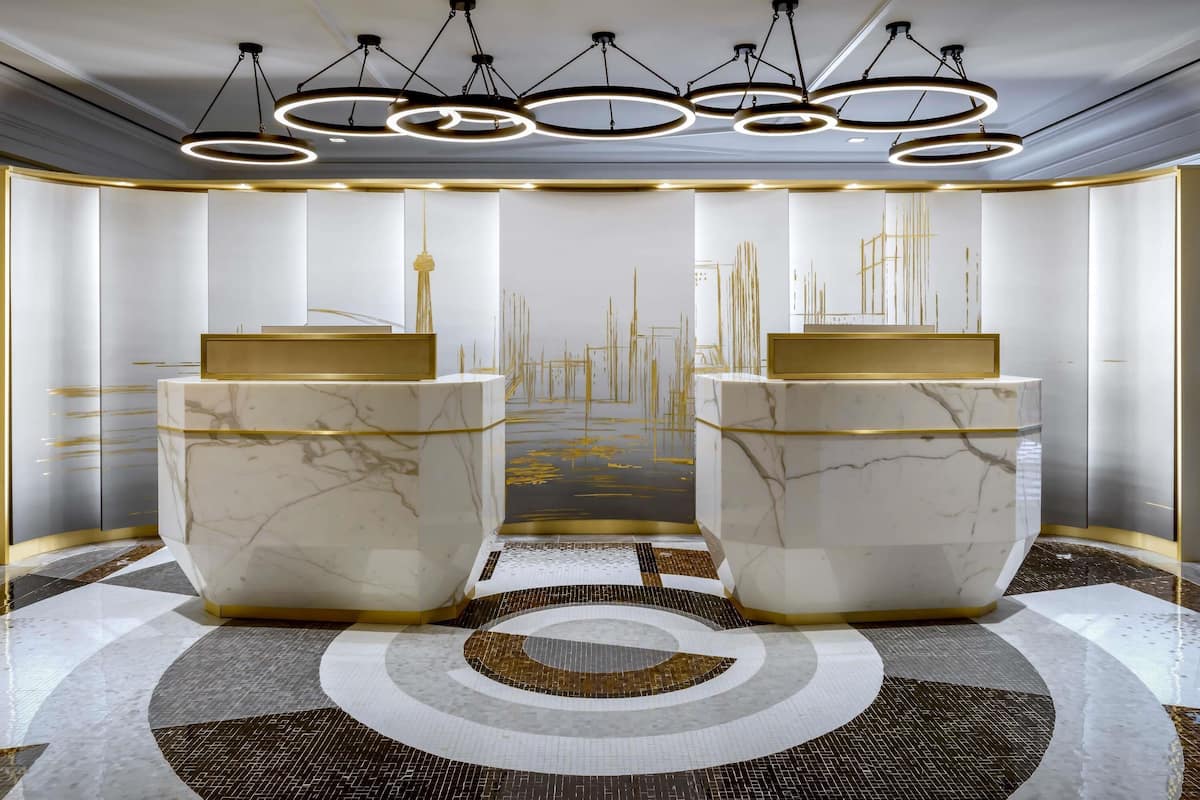 A modern hotel lobby with marble reception desks, a circular patterned floor, and a cityscape mural on the wall.