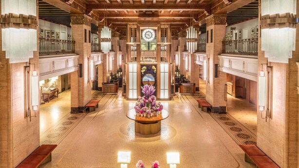 A grand lobby with a central clock, ornate ceiling, and a reception desk with a floral arrangement. - Fairmont Royal York Gold Experience (Toronto)