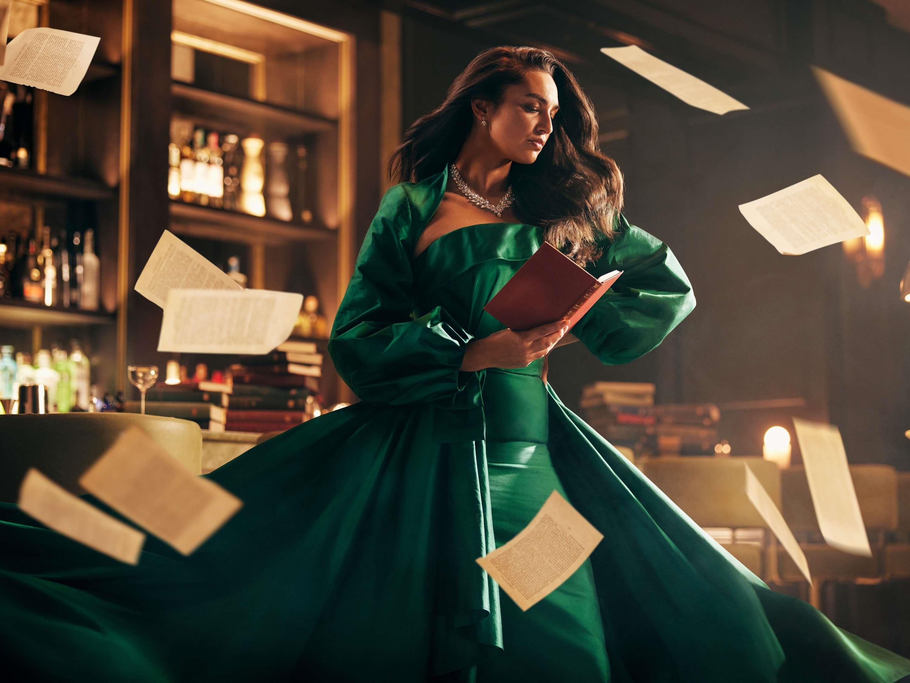 A person in a green dress holding a book with papers flying around.