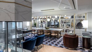 Una sala moderna con un separador de vidrio, un comedor con una mesa grande y sillas, y una cocina con estanterías y una mesa redonda.