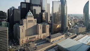 A cityscape with a variety of high-rise buildings, including a prominent building with a green roof and the text "Fifth Avenue Hotel." - Fairmont Royal York Gold Experience (Toronto)