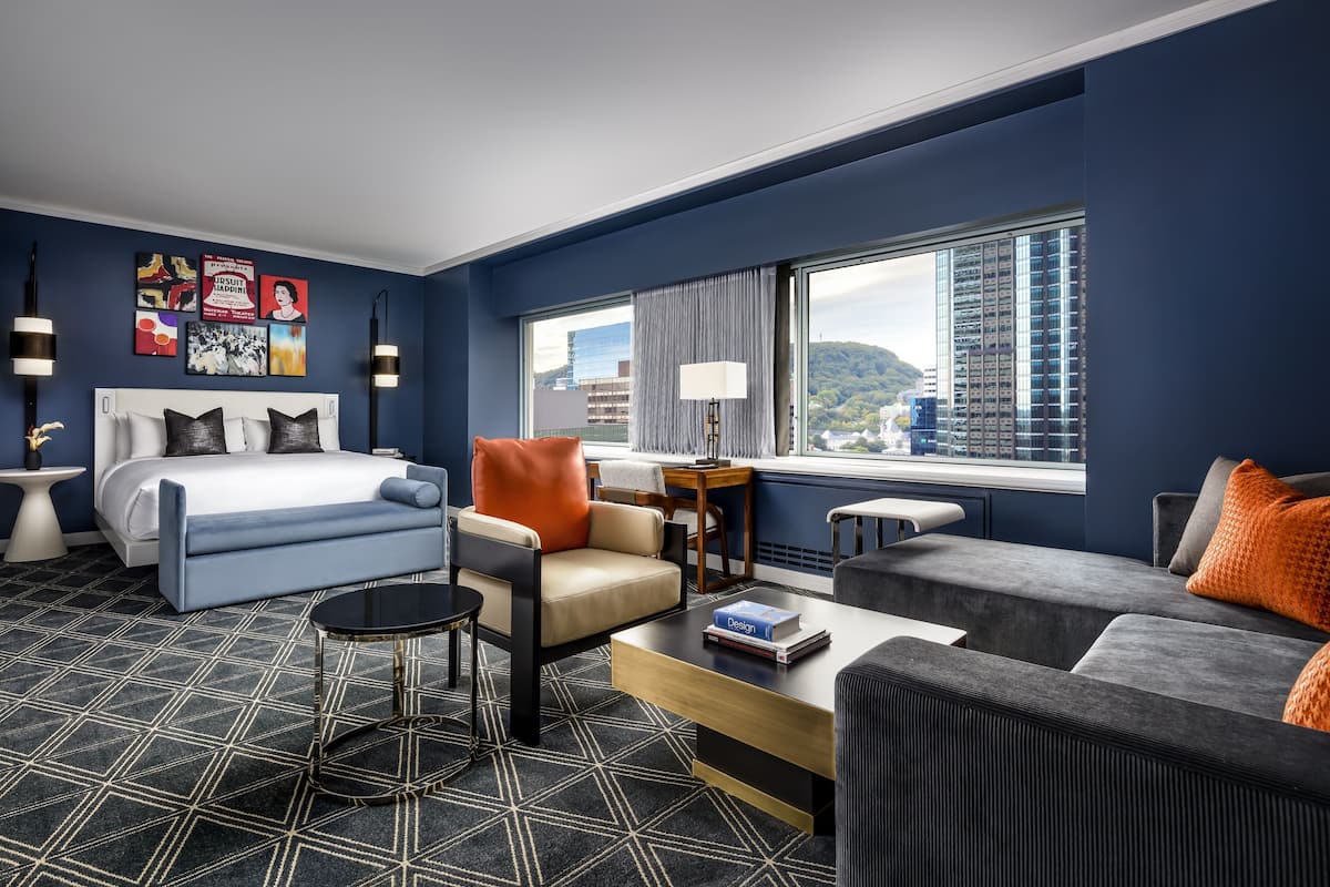A modern hotel room with a large bed, a sofa, a coffee table, and a view of the cityscape.