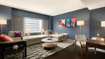 Un salon moderne avec un ensemble de canapés, une table basse et une table à manger. On y trouve deux lampes, un tapis et des œuvres d’art accrochées au mur.