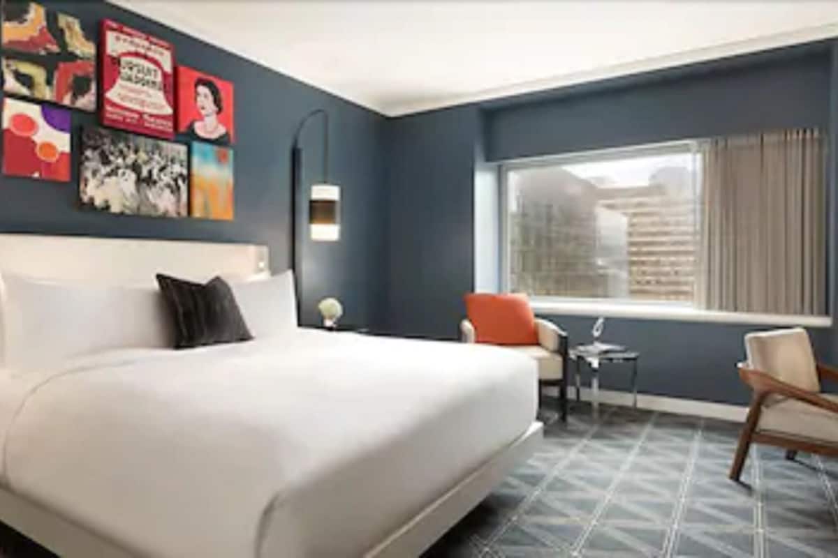 A hotel room with a large bed, a desk, a chair, and a window with a view of buildings.