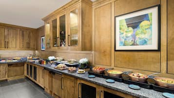 A spacious kitchen with wooden cabinets, a granite countertop, and various food items displayed.