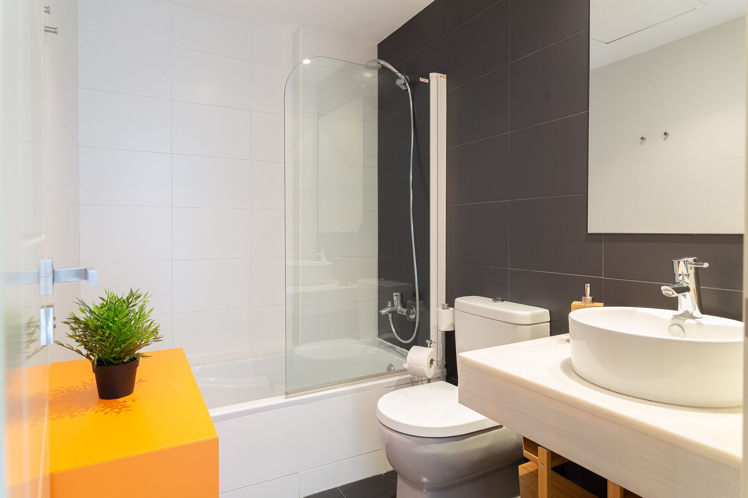 A modern bathroom with a glass-enclosed shower, a white toilet, and a sink with a mirror above.