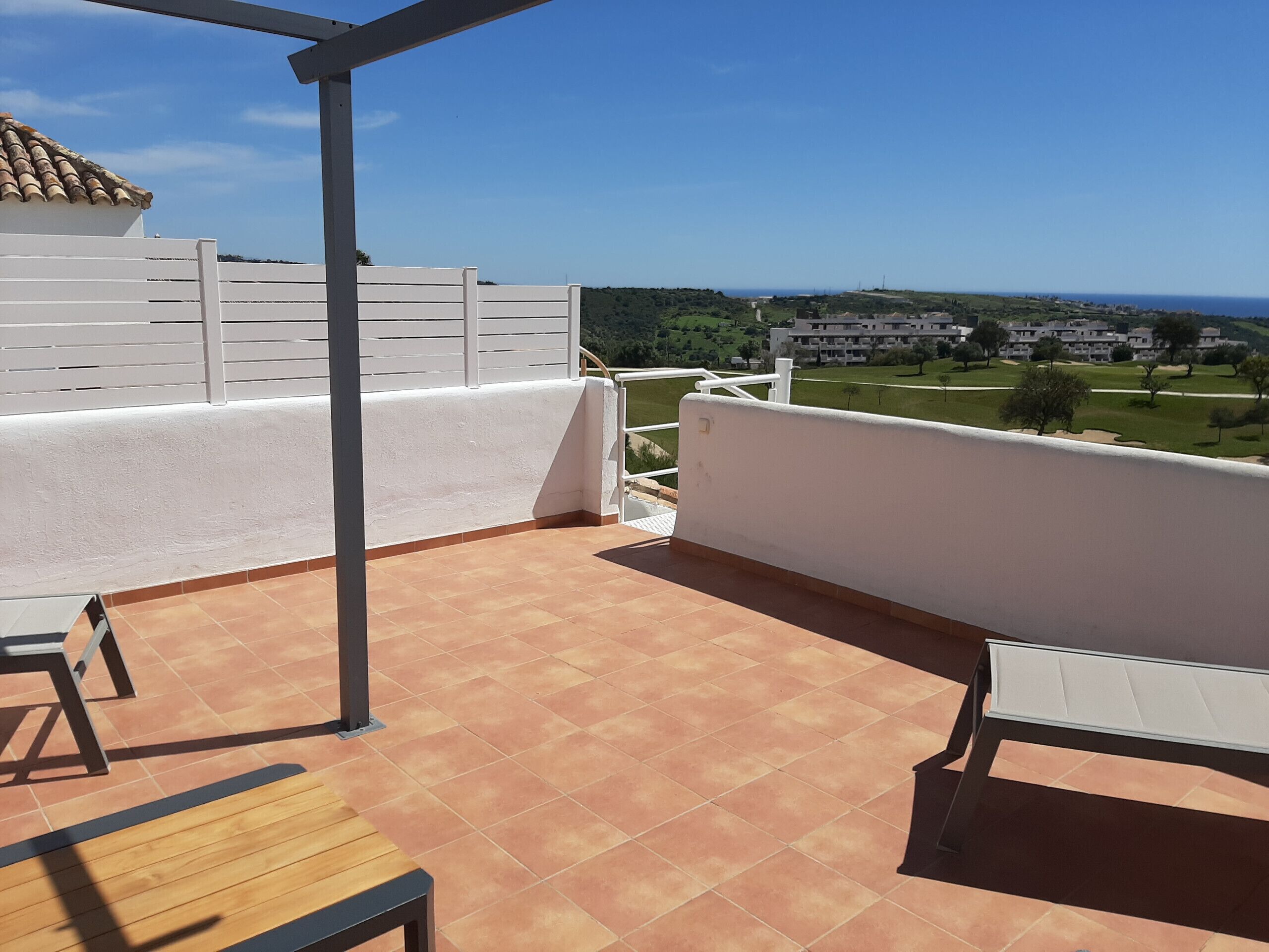 A terrace with a tiled floor, white railing, and a view of a residential area.
