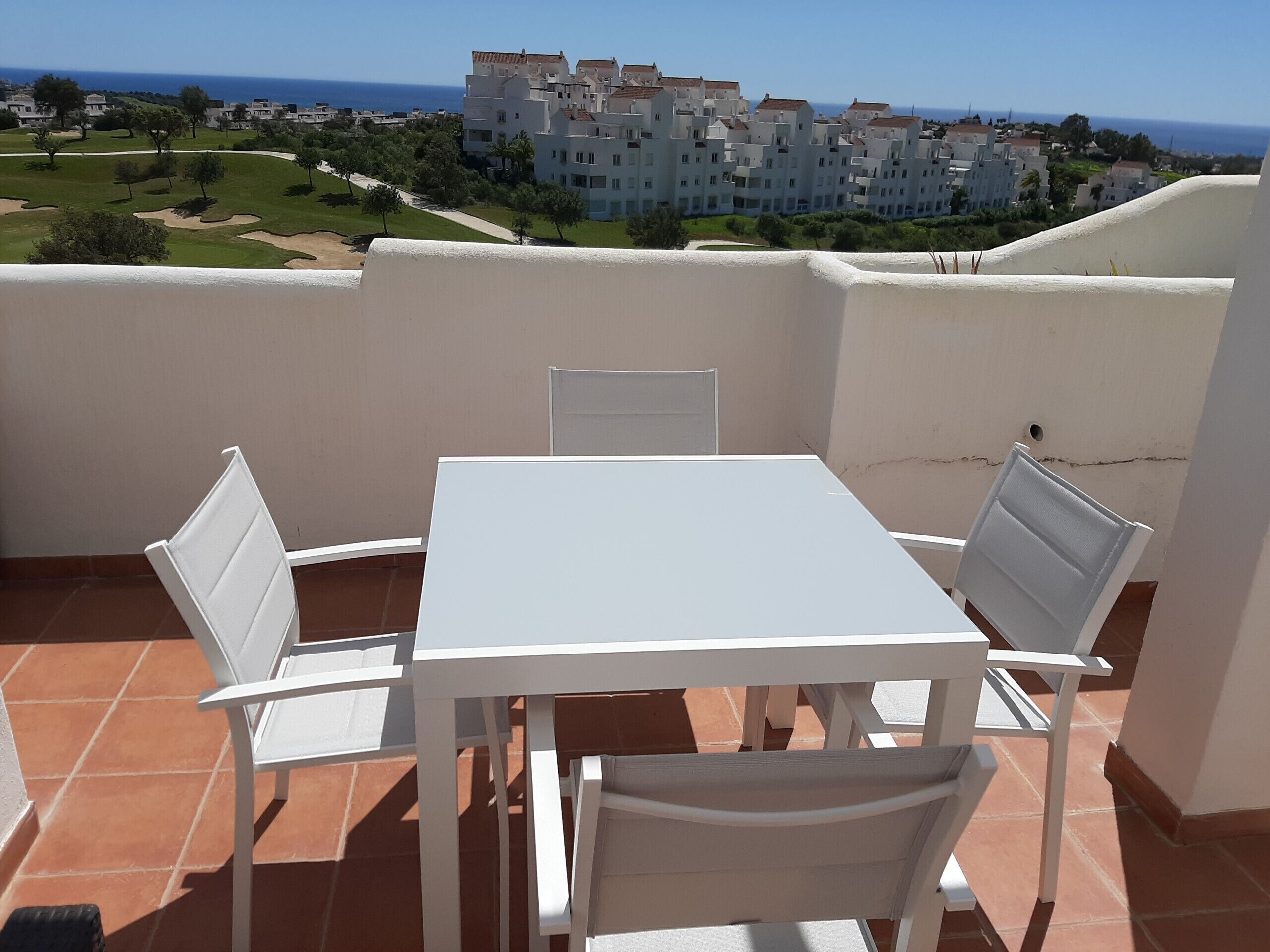 A terrace with a white table and chairs, overlooking a coastal residential area.