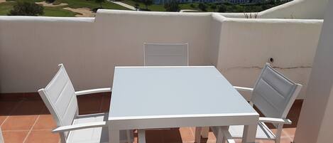 A terrace with a white table and chairs, overlooking a coastal residential area.