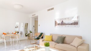 A modern living room with a beige sofa, a glass coffee table, and a dining area with a white table and chairs. - Valle Romano Prestigious 2266 (Estepona)