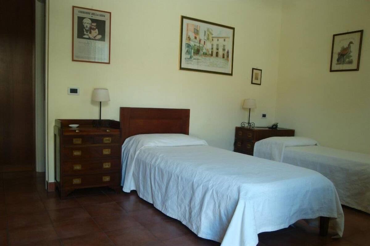 A hotel room with two single beds, a wooden dresser, and a nightstand with a lamp.