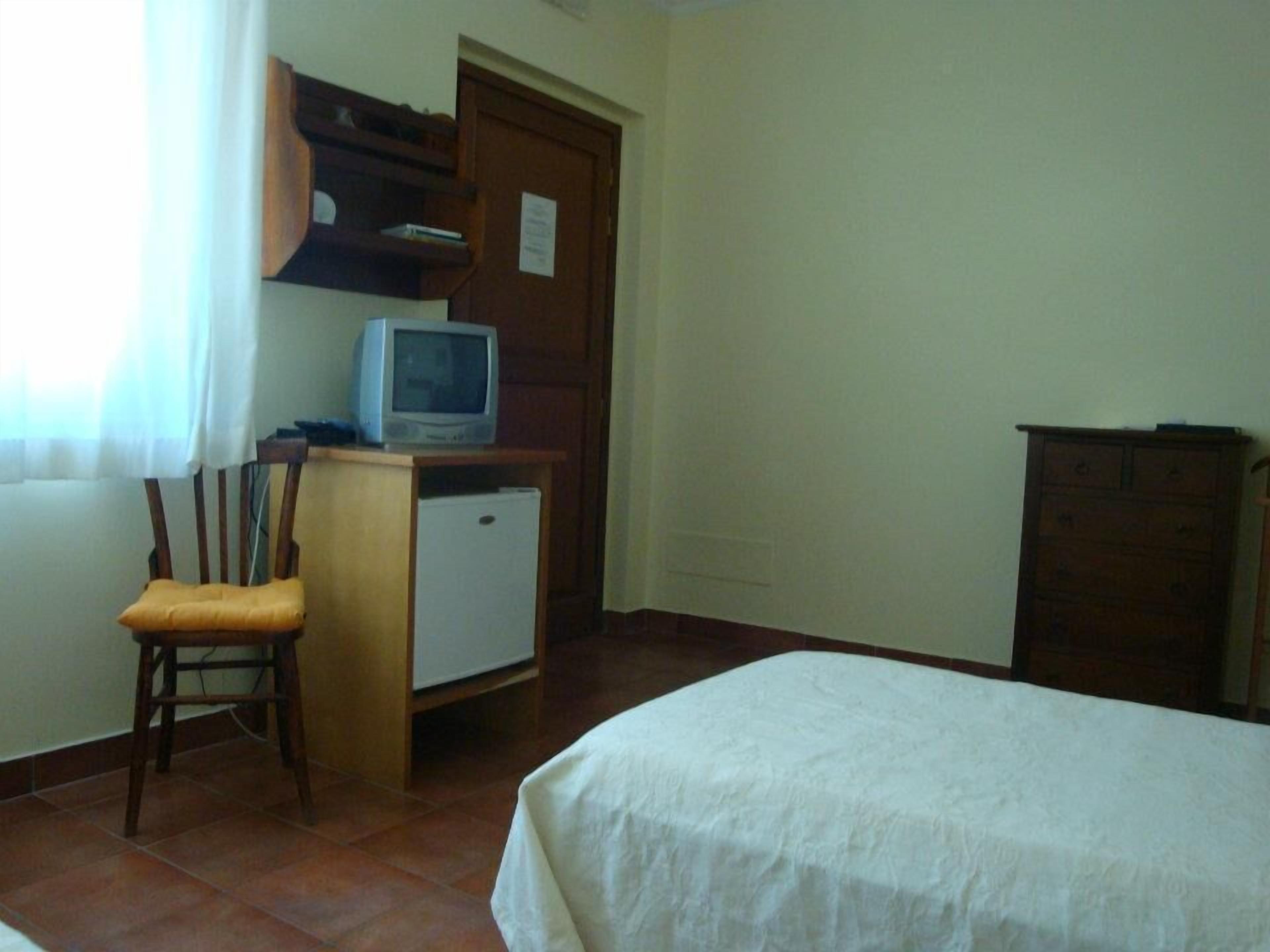 Una stanza con un letto, una scrivania con computer e televisione, una sedia e un armadio.