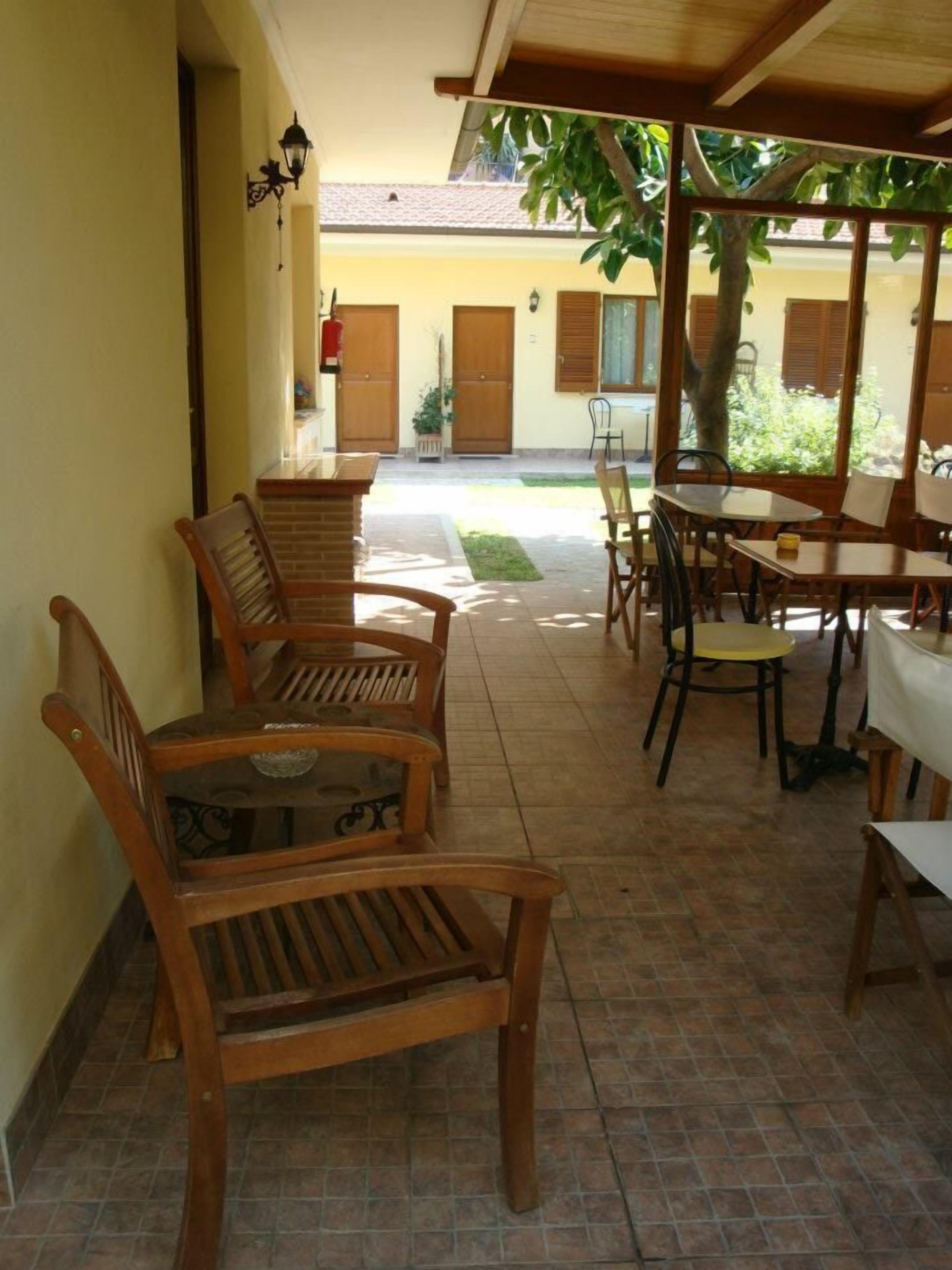 Ein überdachter Patio-Bereich mit Holzmöbeln, darunter Stühle und ein Tisch, und einem gefliesten Boden.