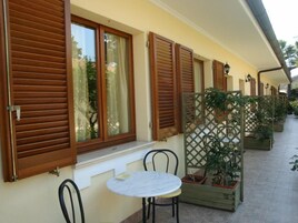 Un balcón con contraventanas de madera, una mesa redonda y plantas en macetas.