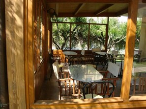 A covered outdoor seating area with wooden tables and chairs, surrounded by glass walls and wooden beams. - Villa Anita (Fondi)
