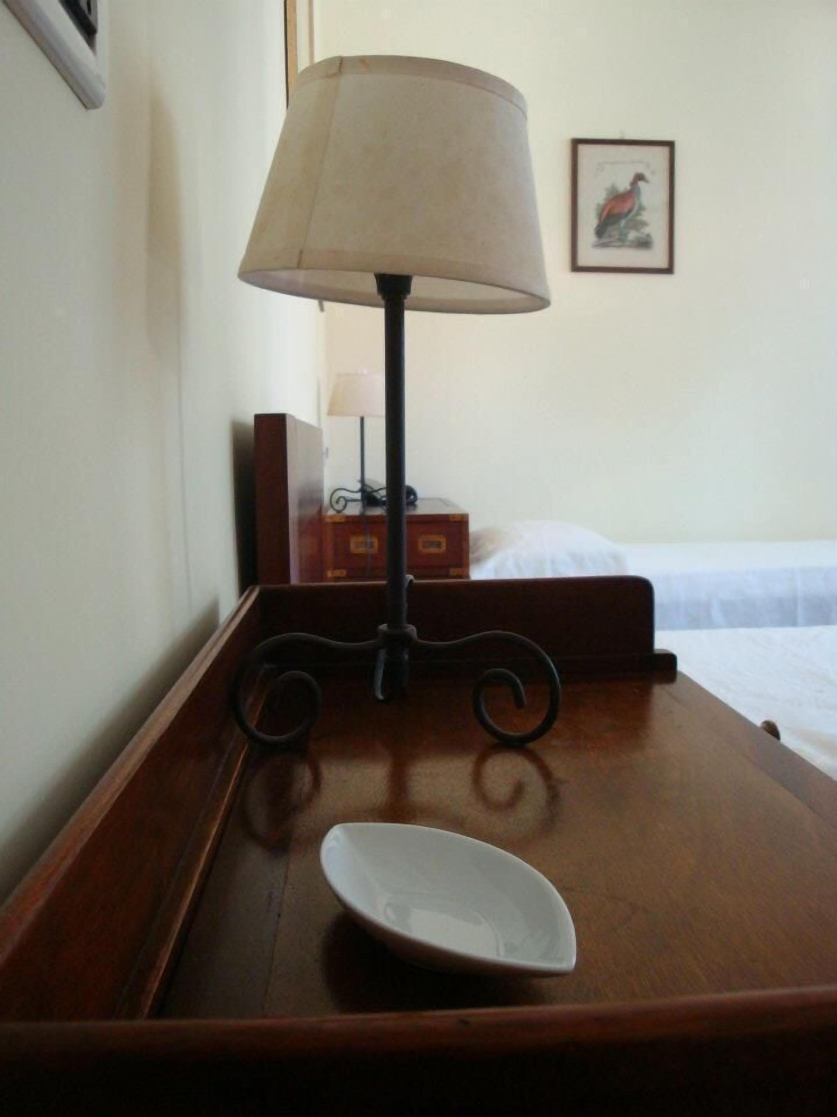 A wooden bedside table with a white plate, a lamp, and a framed picture on the wall.