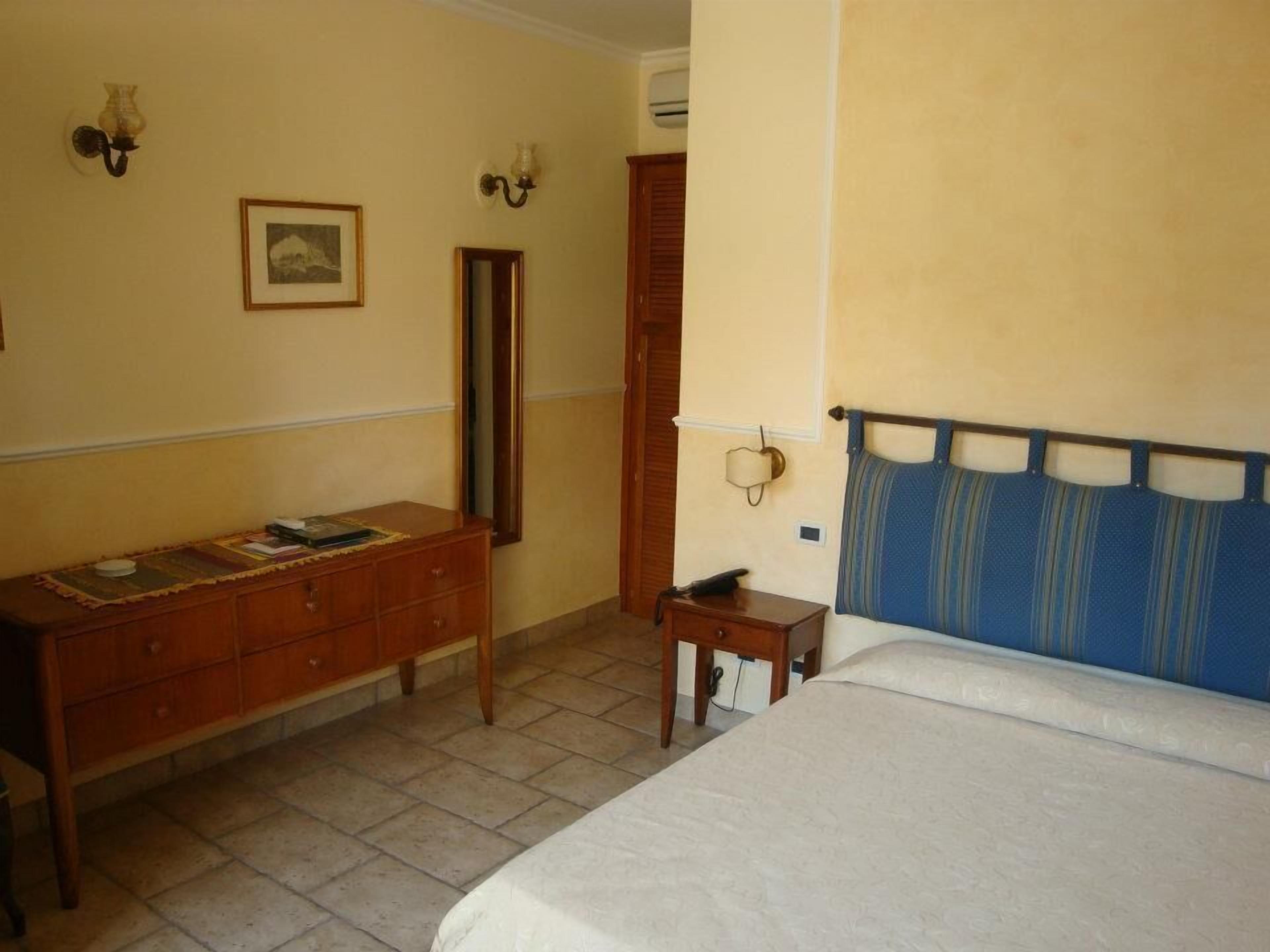 A bedroom with a bed, a wooden dresser, a mirror, and a small bedside table.