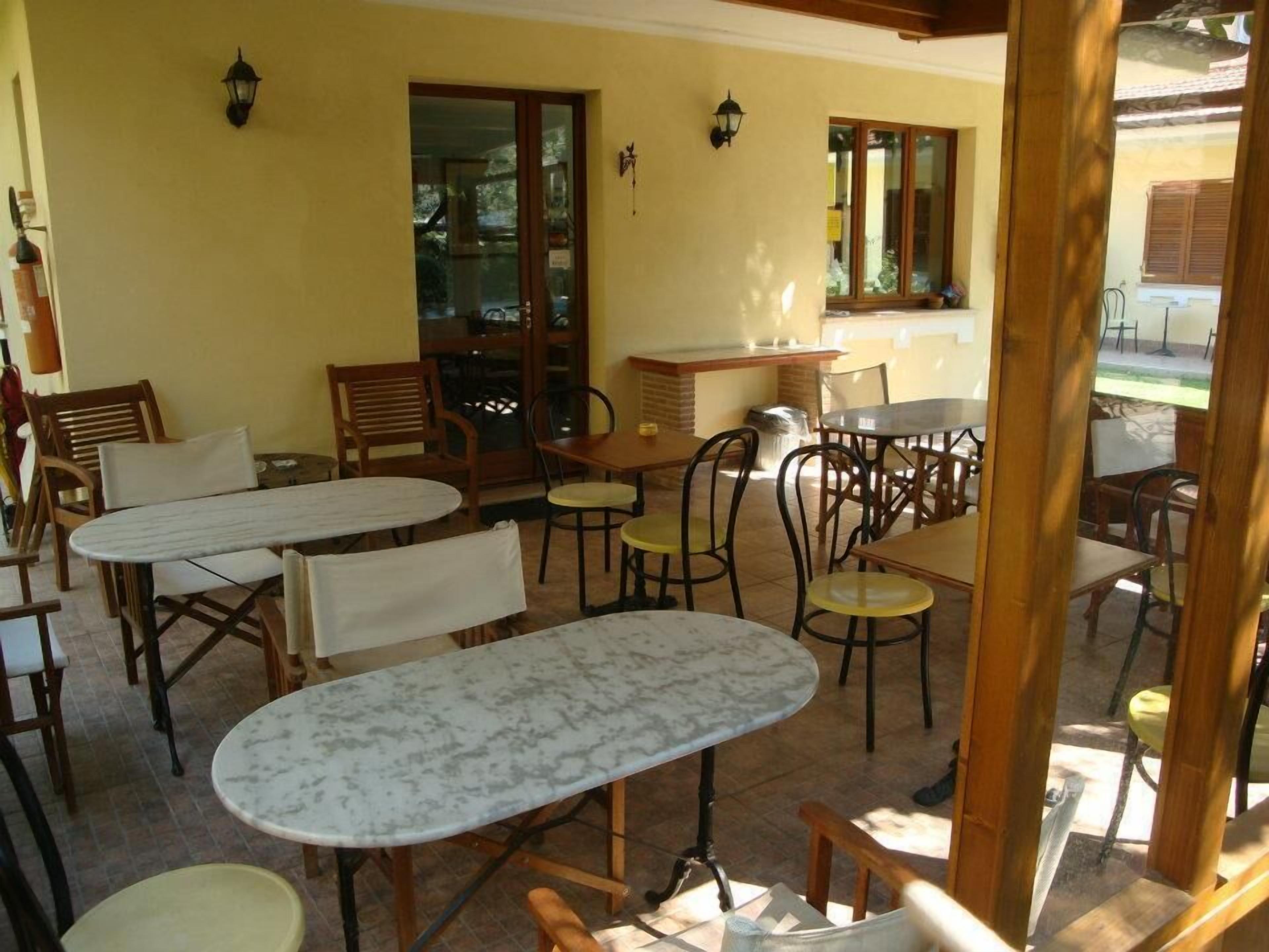 An outdoor patio area with multiple tables and chairs, a wooden pergola, and a glass door leading to a garden.