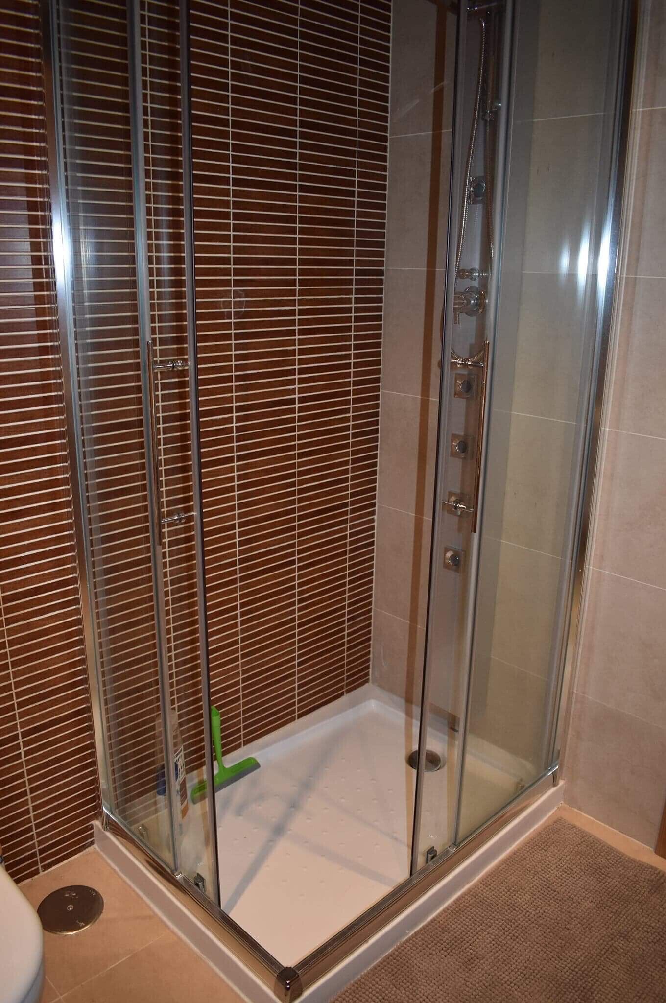 Ducha con paredes de vidrio, suelo de azulejos y agarradera metálica.