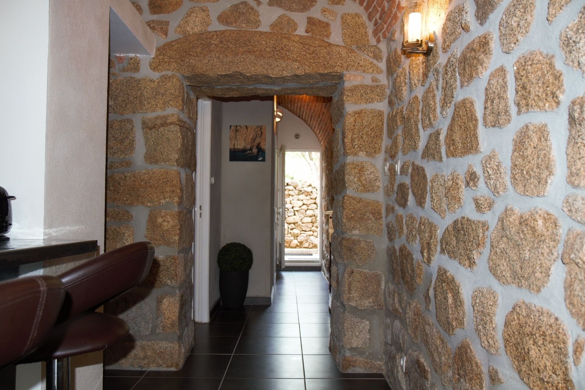 Un couloir aux murs de pierre, avec un banc et une porte donnant sur un escalier en pierre.