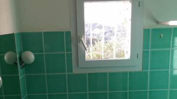 Een badkamer met groene tegels, een witte wastafel en een raam boven de spiegel.