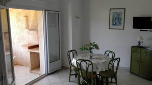 A dining area with a table, chairs, a vase with flowers, a cabinet, and a television on the wall. - Mini-villa No. 2 - 2/4 people (PORTO VECCHIO)