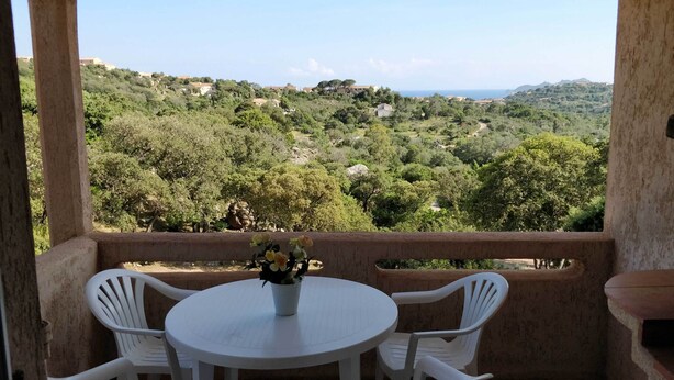 A balcony with a table and chairs, overlooking a lush green landscape with hills and a clear sky. - Mini-villa No. 2 - 2/4 people (PORTO VECCHIO)
