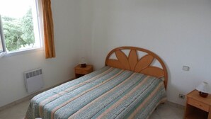 A bedroom with a bed, a window with curtains, a bedside table with a lamp, and a heater. - Mini-villa No. 2 - 2/4 people (PORTO VECCHIO)