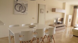 A modern dining area with a white table and chairs, a decorative bowl, and a flat-screen TV on a cabinet.