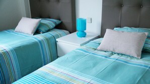 A hotel room with two beds, each with striped bedding and pillows. There is a white nightstand with a blue lamp between the beds.