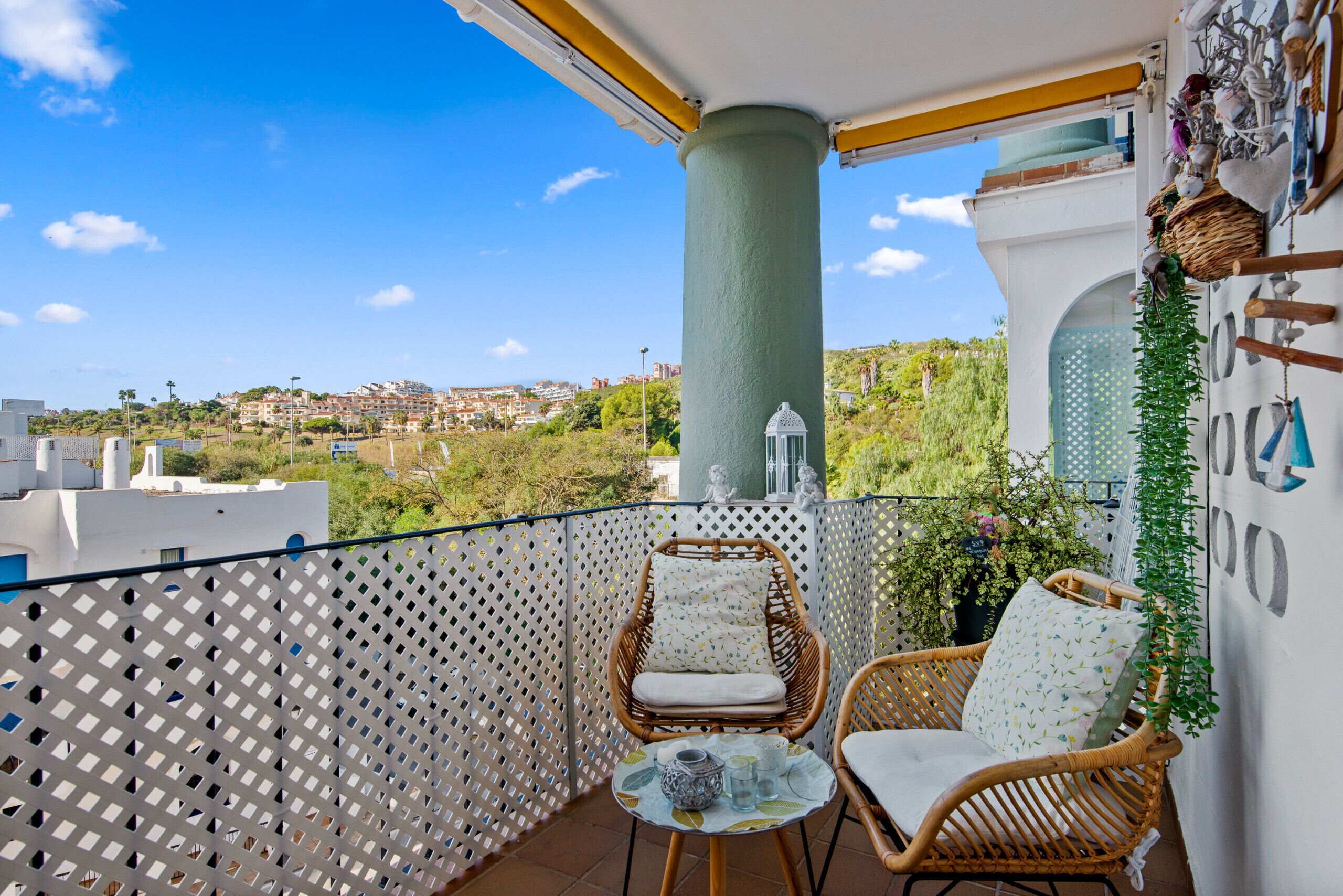 Ein Balkon mit Korbstühlen, einem kleinen Tisch und Blick auf eine Stadt.