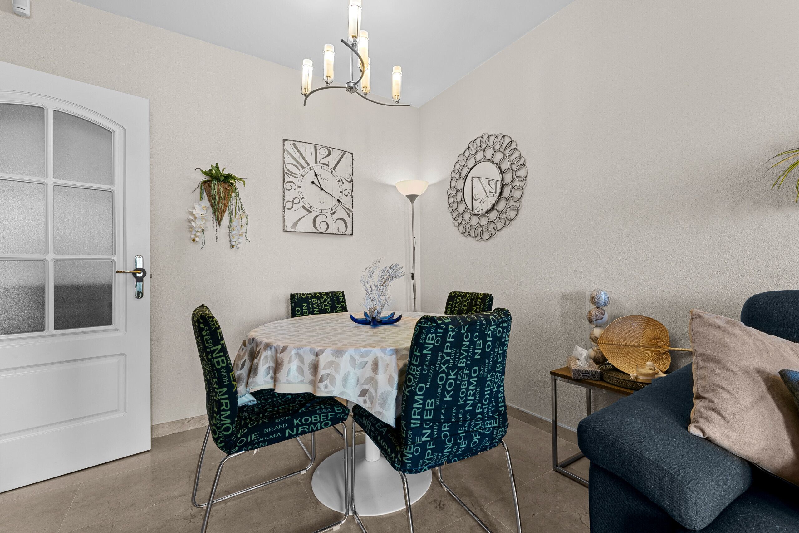 Un comedor con una mesa redonda, sillas, una araña, detalles decorativos en la pared y un sofá.