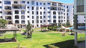 A multi-story hotel with balconies, a swimming pool, and a well-maintained lawn with seating areas. - Marina Duquesa 2110 Lovely Place (Manilva)
